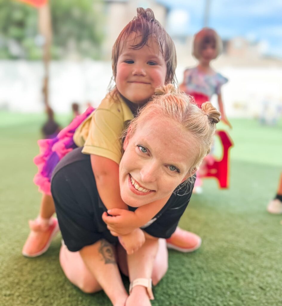 Teacher and preschool child smiling together during outdoor playtime